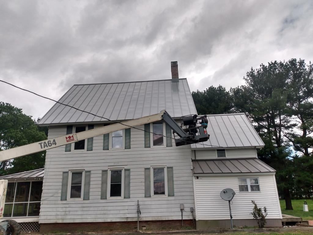A white house with a metal roof is being cleaned by a crane.