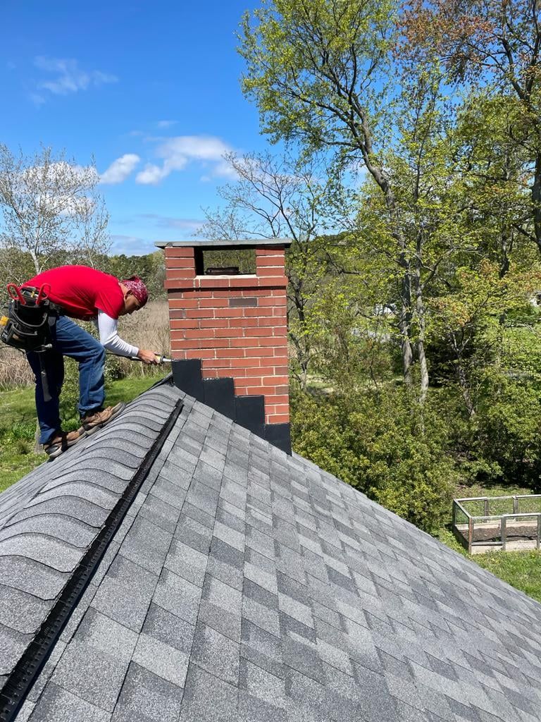 A man is working on a chimney on the roof of a house.