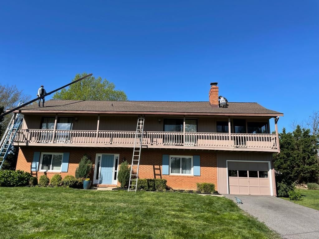 A man is standing on a ladder on the roof of a house.