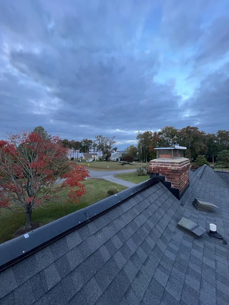 A roof with a chimney on it and a tree in the background.