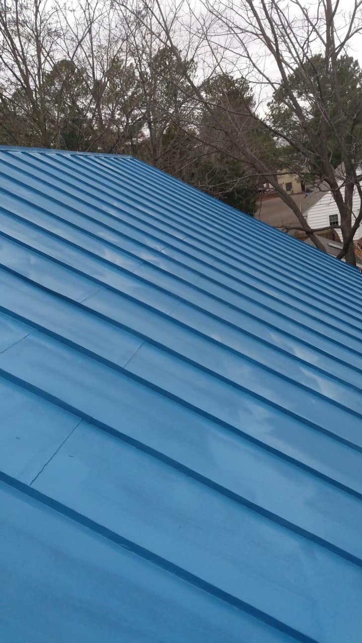 A close up of a blue metal roof with trees in the background.