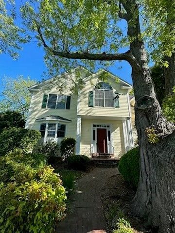 A white house with a red door and a tree in front of it.