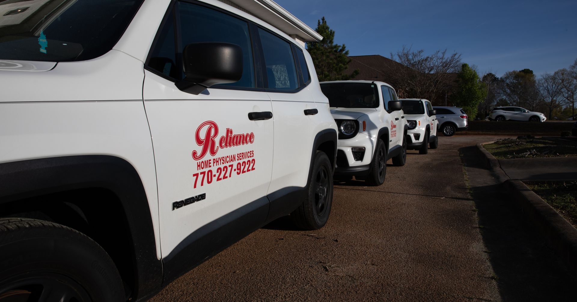A row of white jeeps is parked in a driveway.