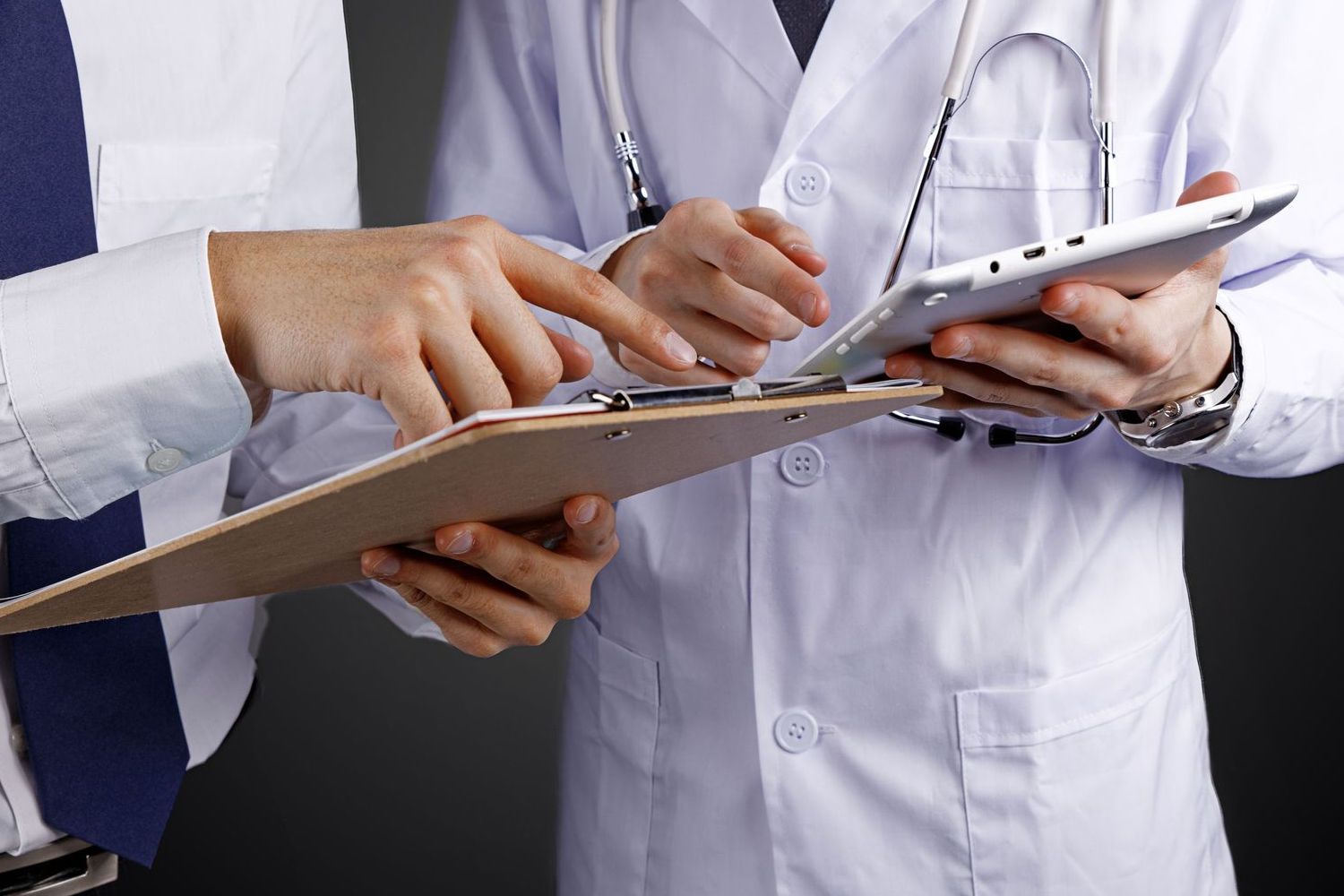 Two doctors are looking at a clipboard and a tablet.