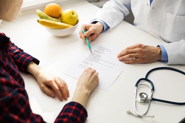 A doctor is talking to a patient who is sitting at a table with a bowl of fruit.