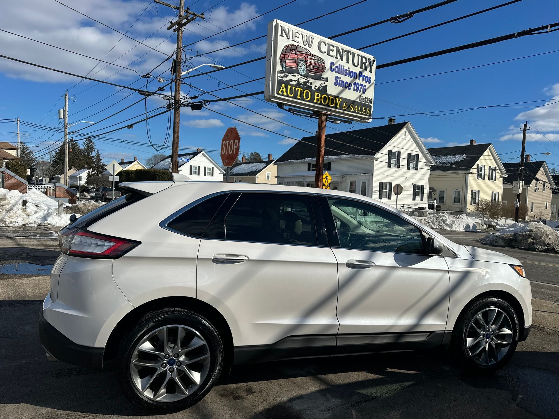 A white SUV was parked in front of a car dealership on a sunny day with snow on the ground.