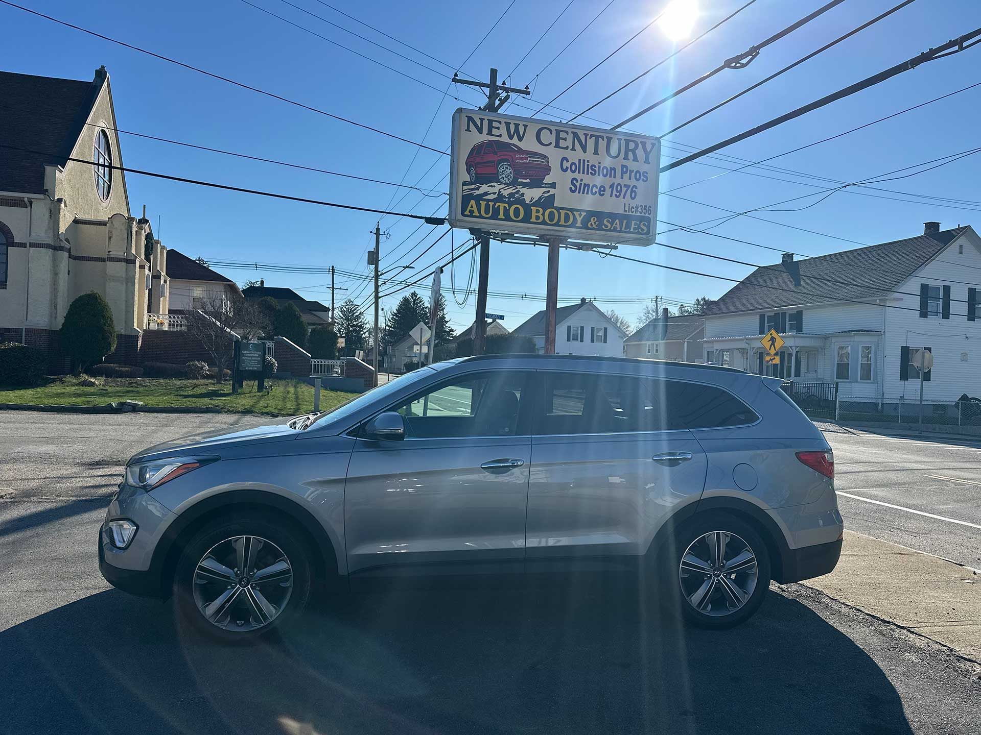 A silver SUV parked in a gravel lot under a bright sun, with a roadside sign and buildings in the background.