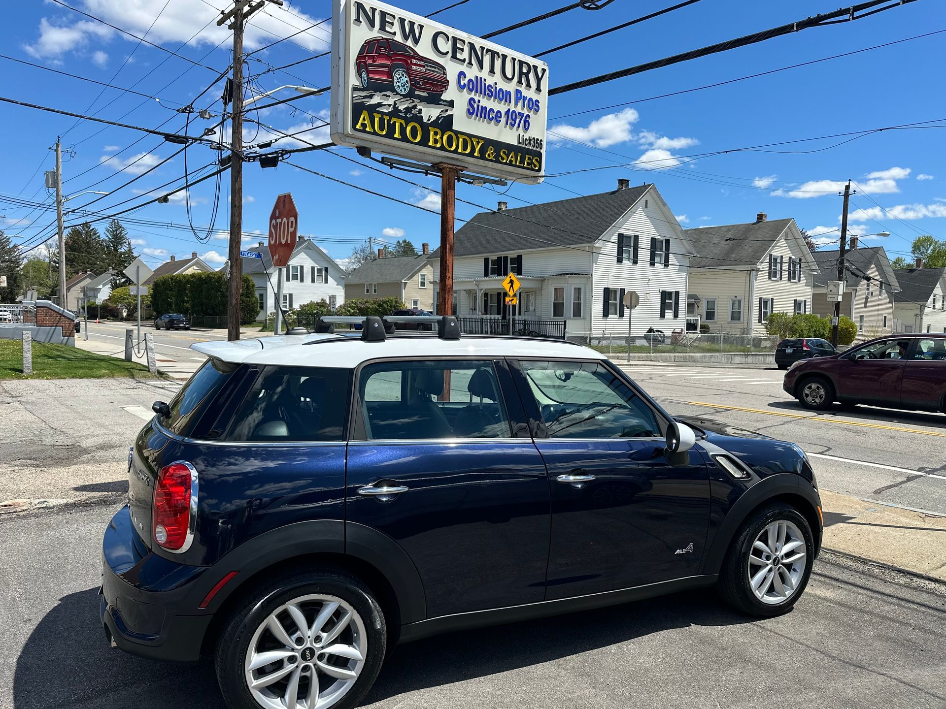 Dark blue Mini Cooper parked near an auto repair shop on a sunny street corner