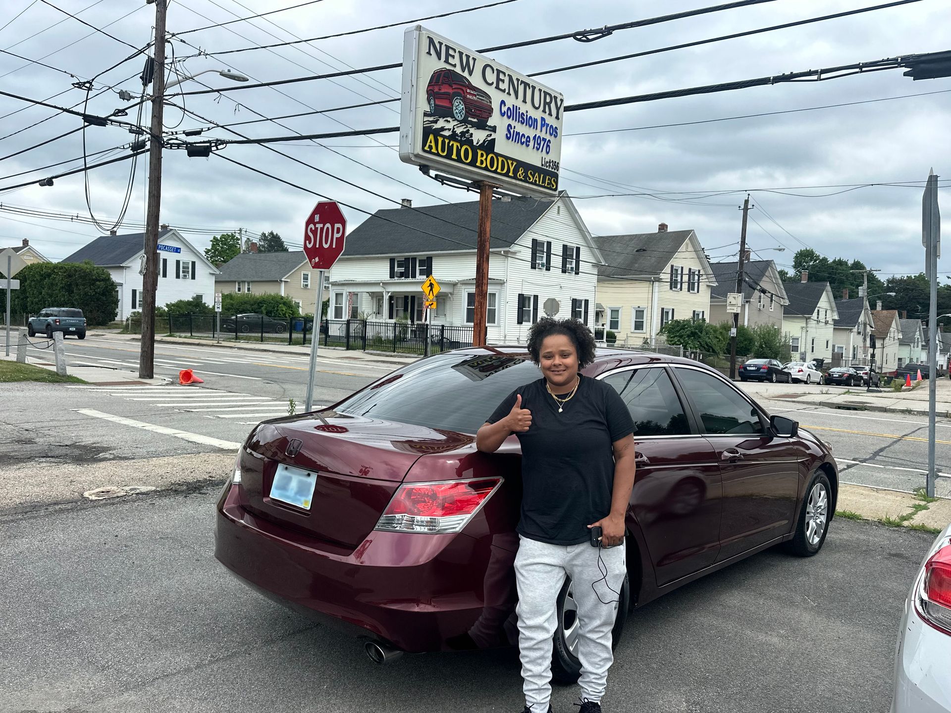 Person standing beside a maroon car at a roadside intersection with a New Century sign in the background