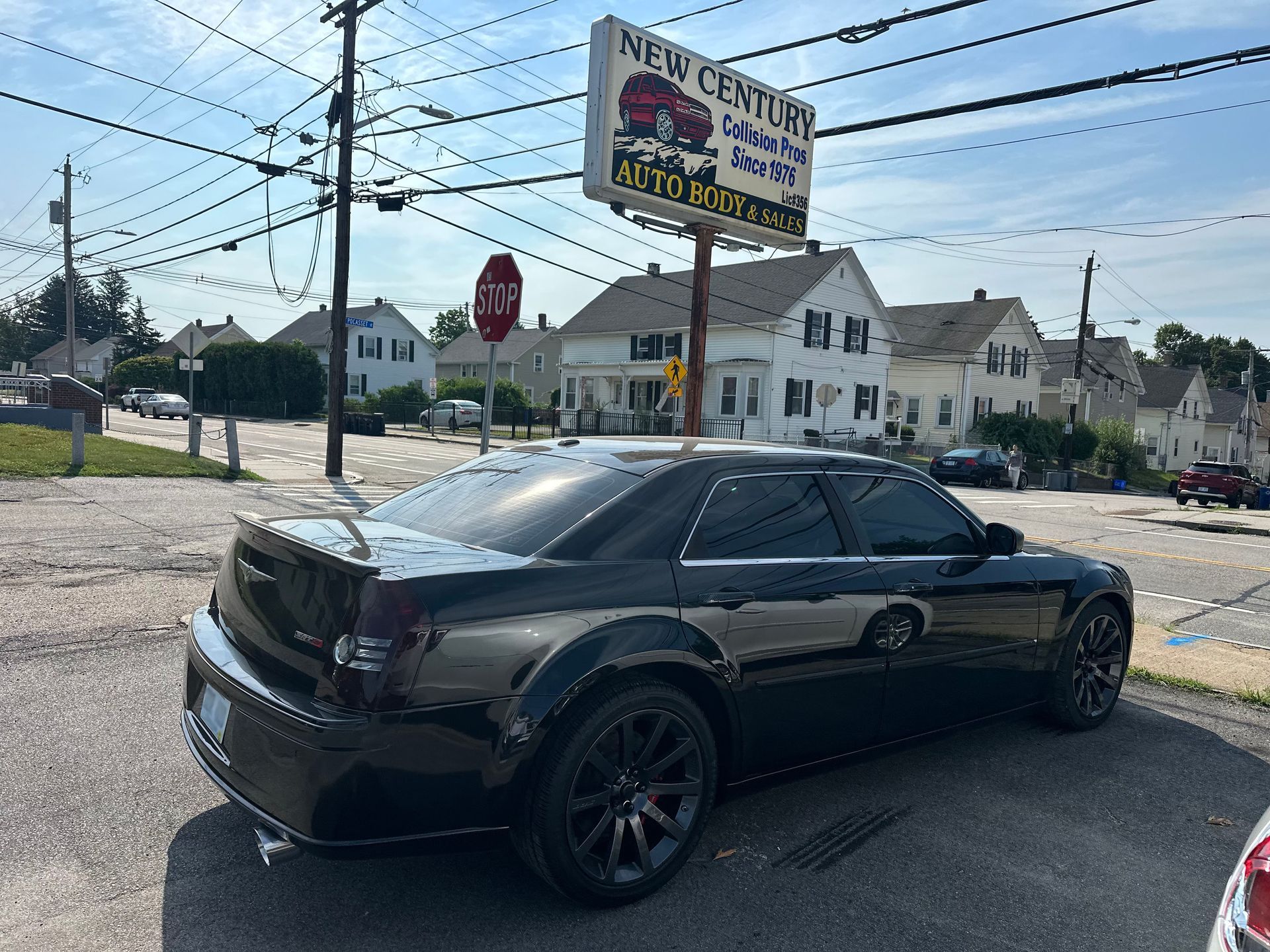 Black sedan parked by a roadside tire shop under a cloudy sky