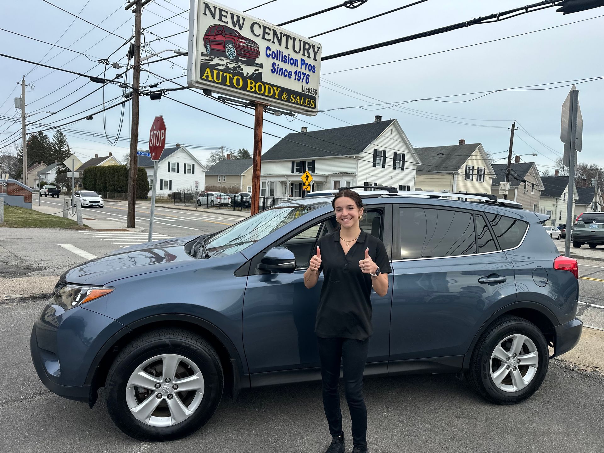 A smiling person gives a thumbs-up next to a blue SUV parked in front of a New Century Auto Body and Glass shop.