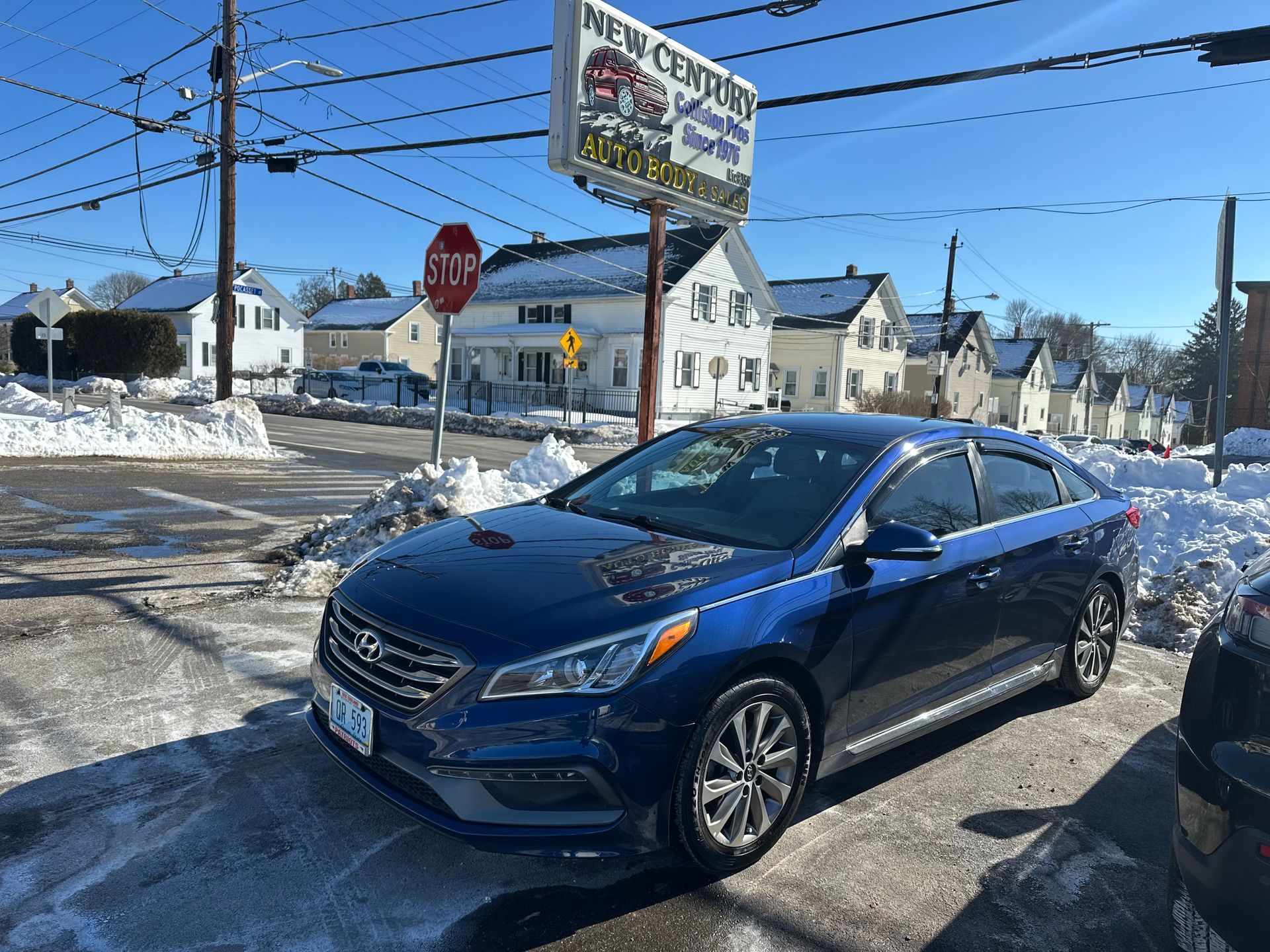 Blue Hyundai Sonata parked on a street with snow. Car dealership sign in the background.