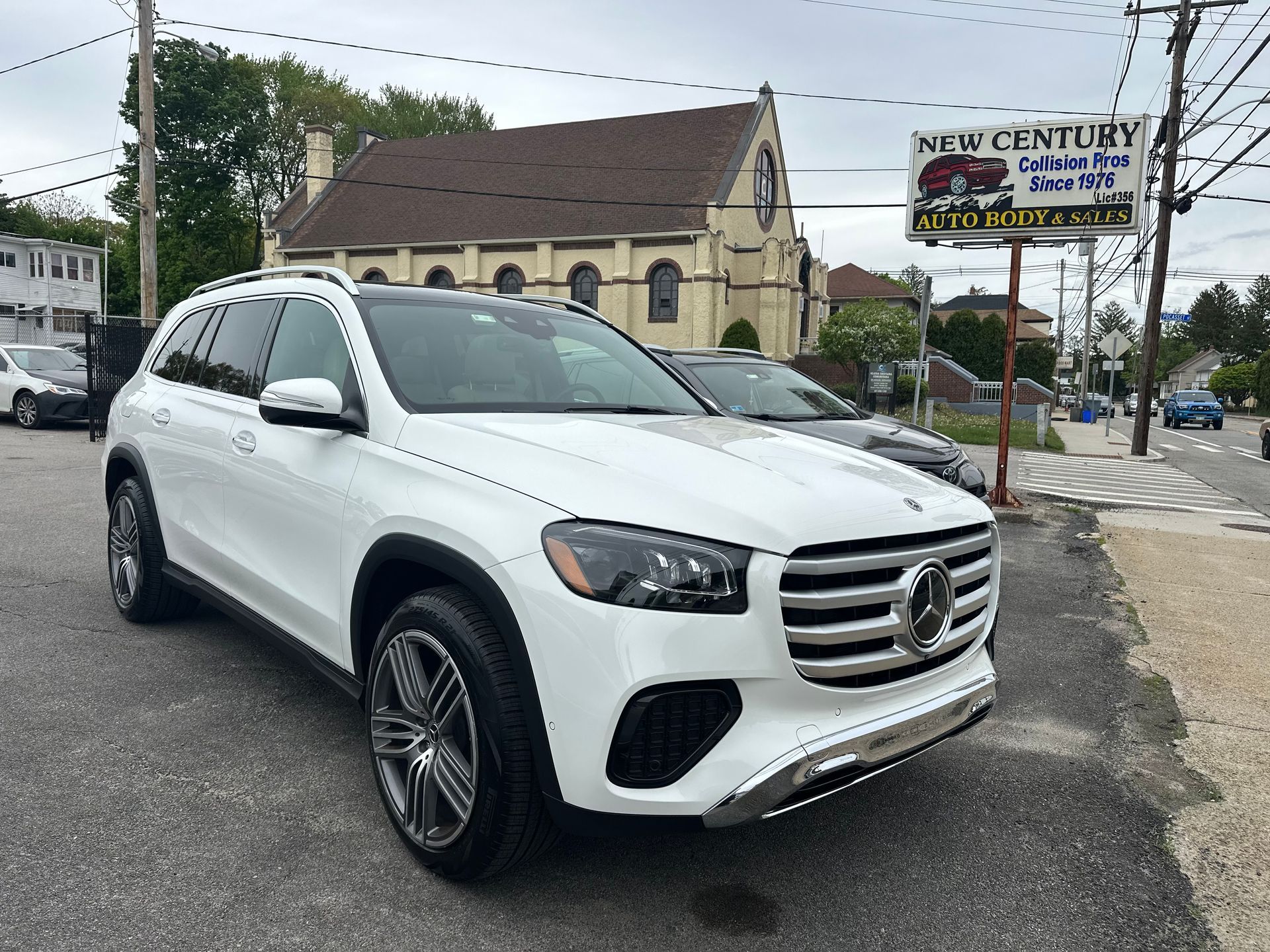 White Mercedes SUV parked on a street near a church and roadside sign.
