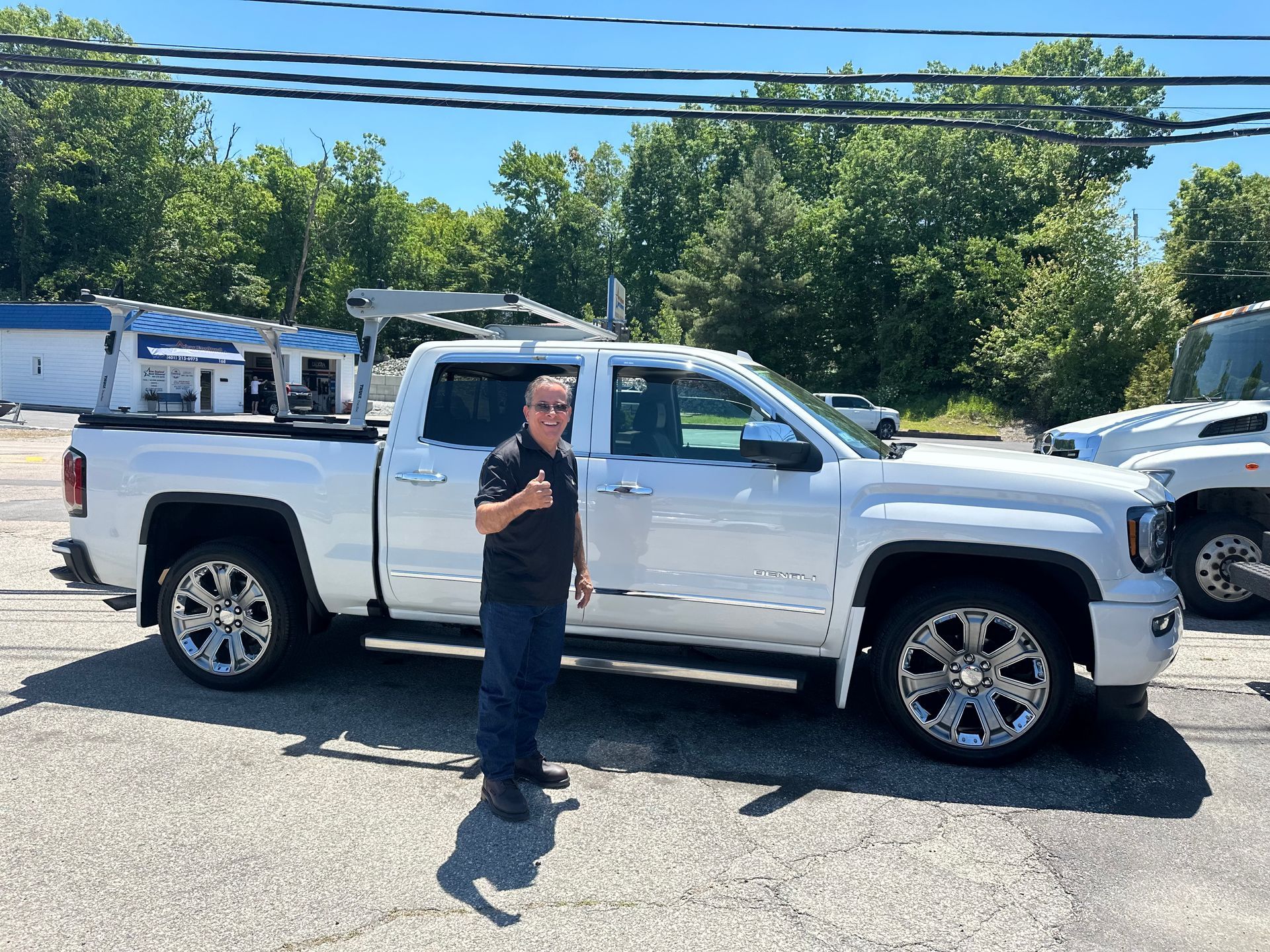 Man standing beside a white pickup truck in a parking lot on a sunny day