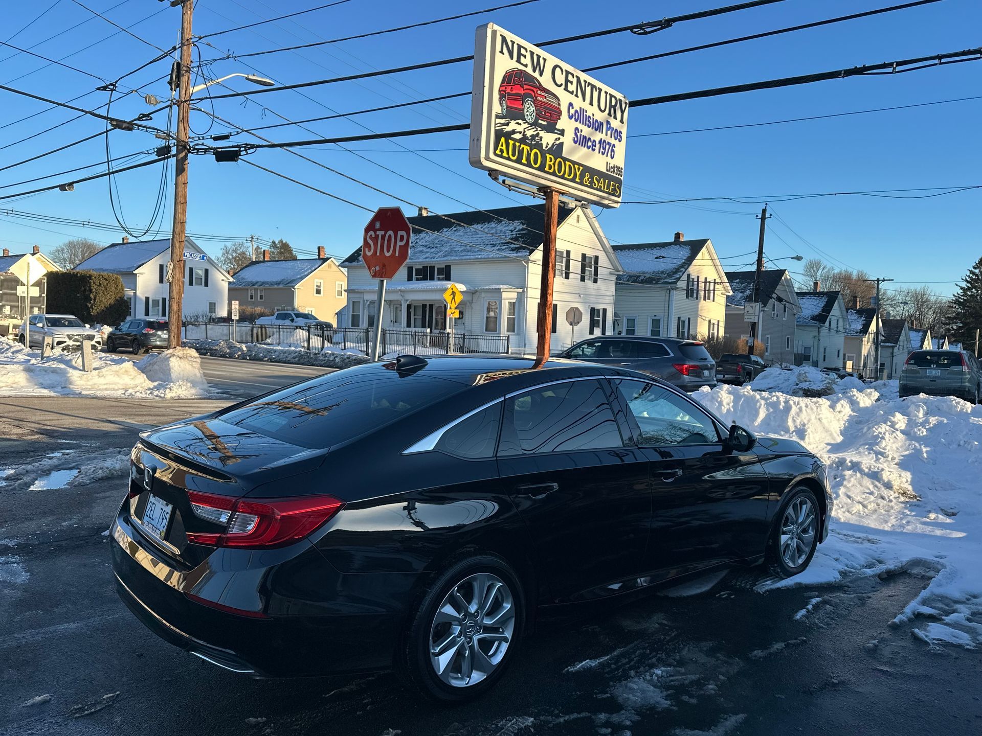 A black car was parked near a car dealership in a snowy residential area.