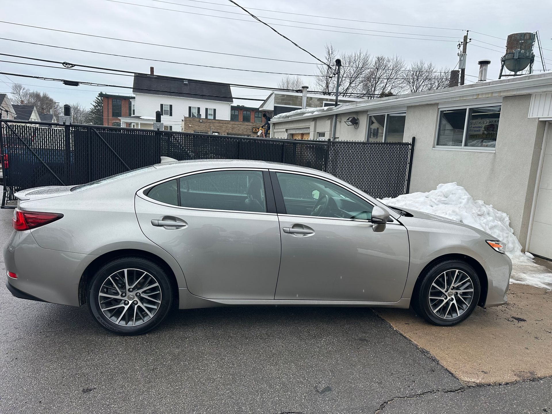 Silver Lexus sedan parked on a wet, gray pavement next to a building with snow.