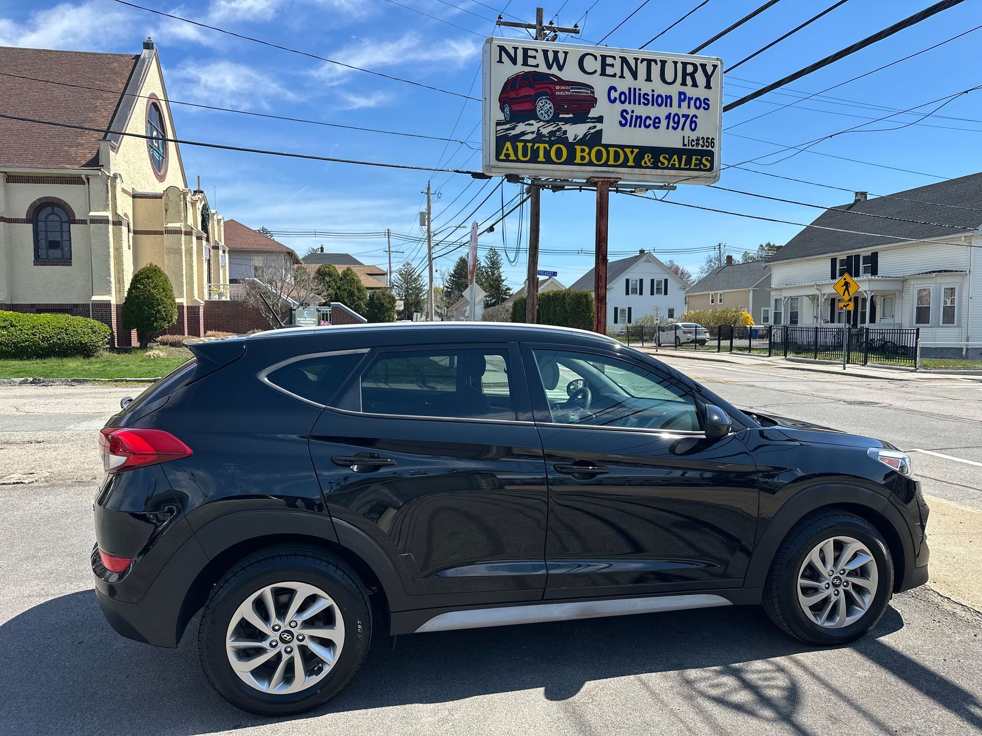 Black compact SUV parked on a sunny street beside a New Century Auto Body sign