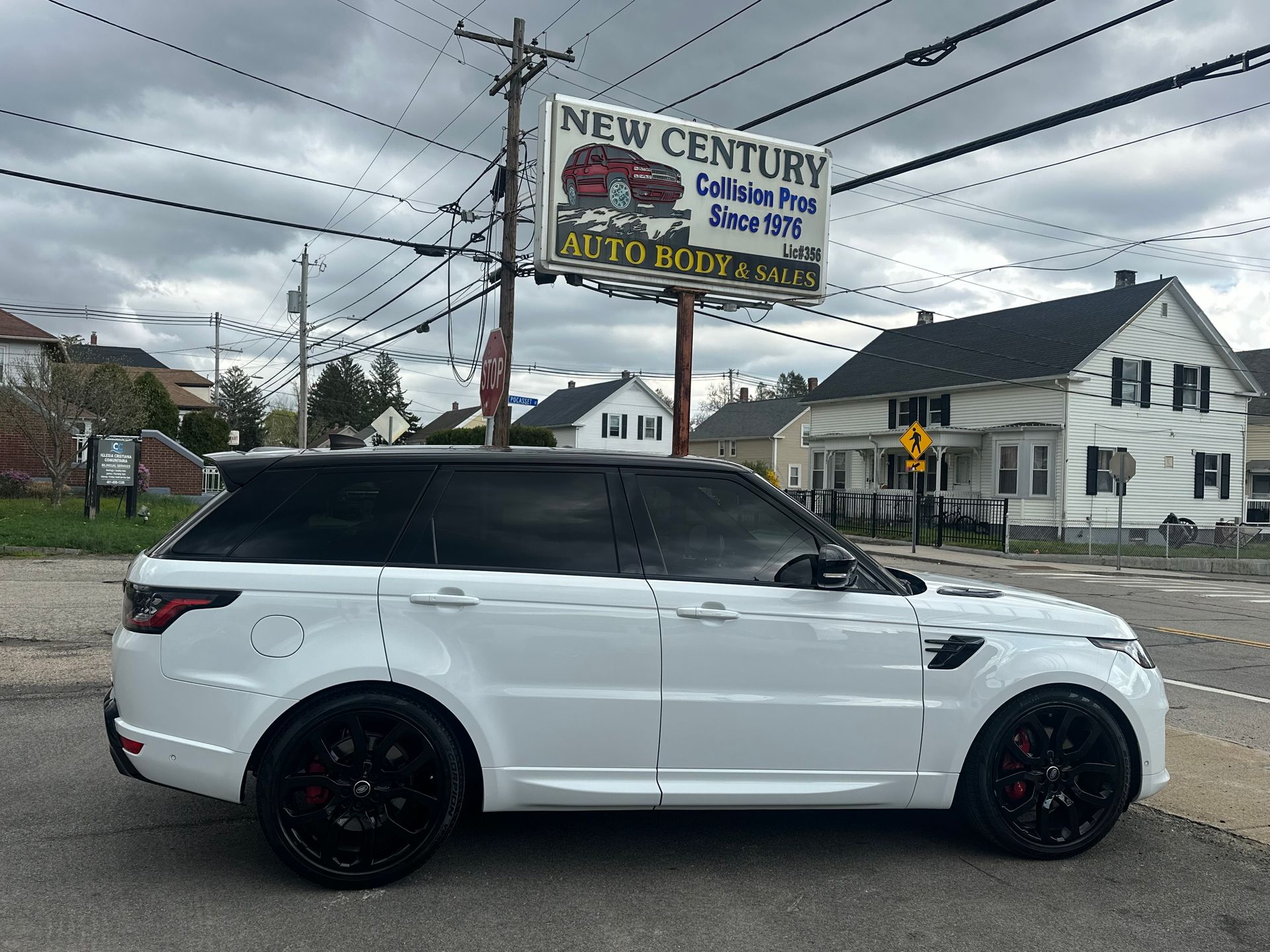White SUV with black wheels parked by a roadside sign under a cloudy sky