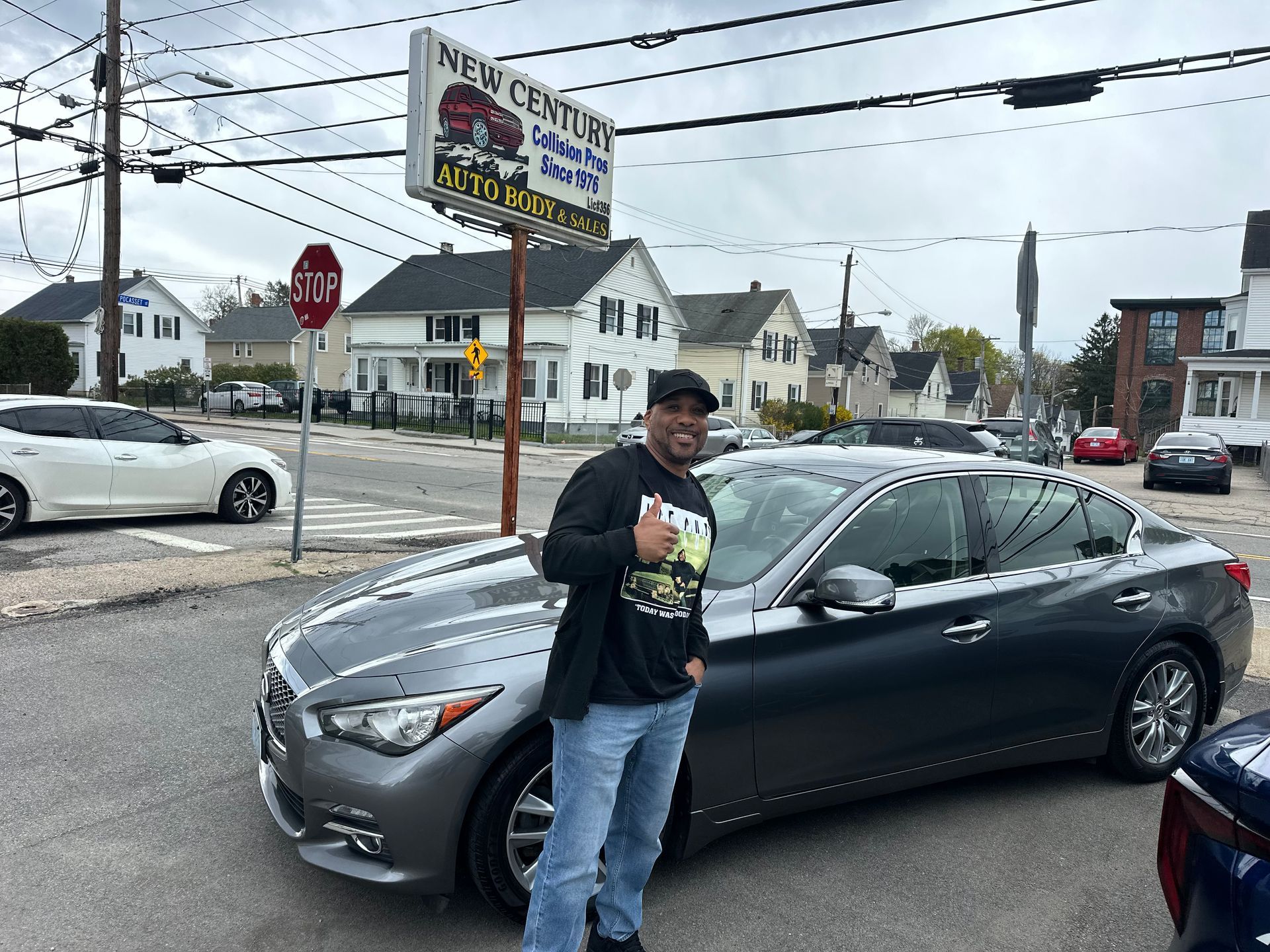 Man standing beside a gray sedan at a busy street intersection with storefronts and traffic lights nearby