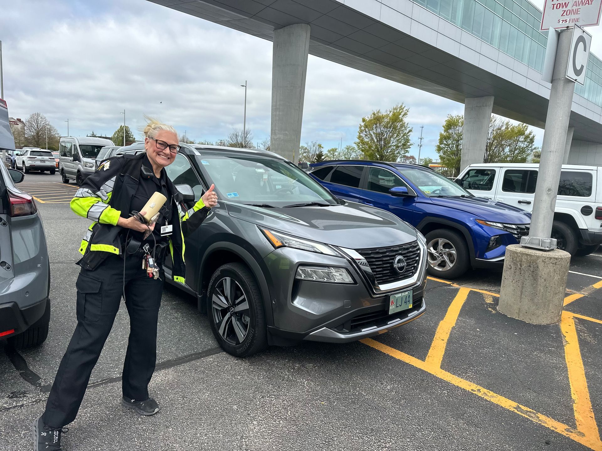 Police officer standing in a parking lot beside a gray SUV under an overpass. 