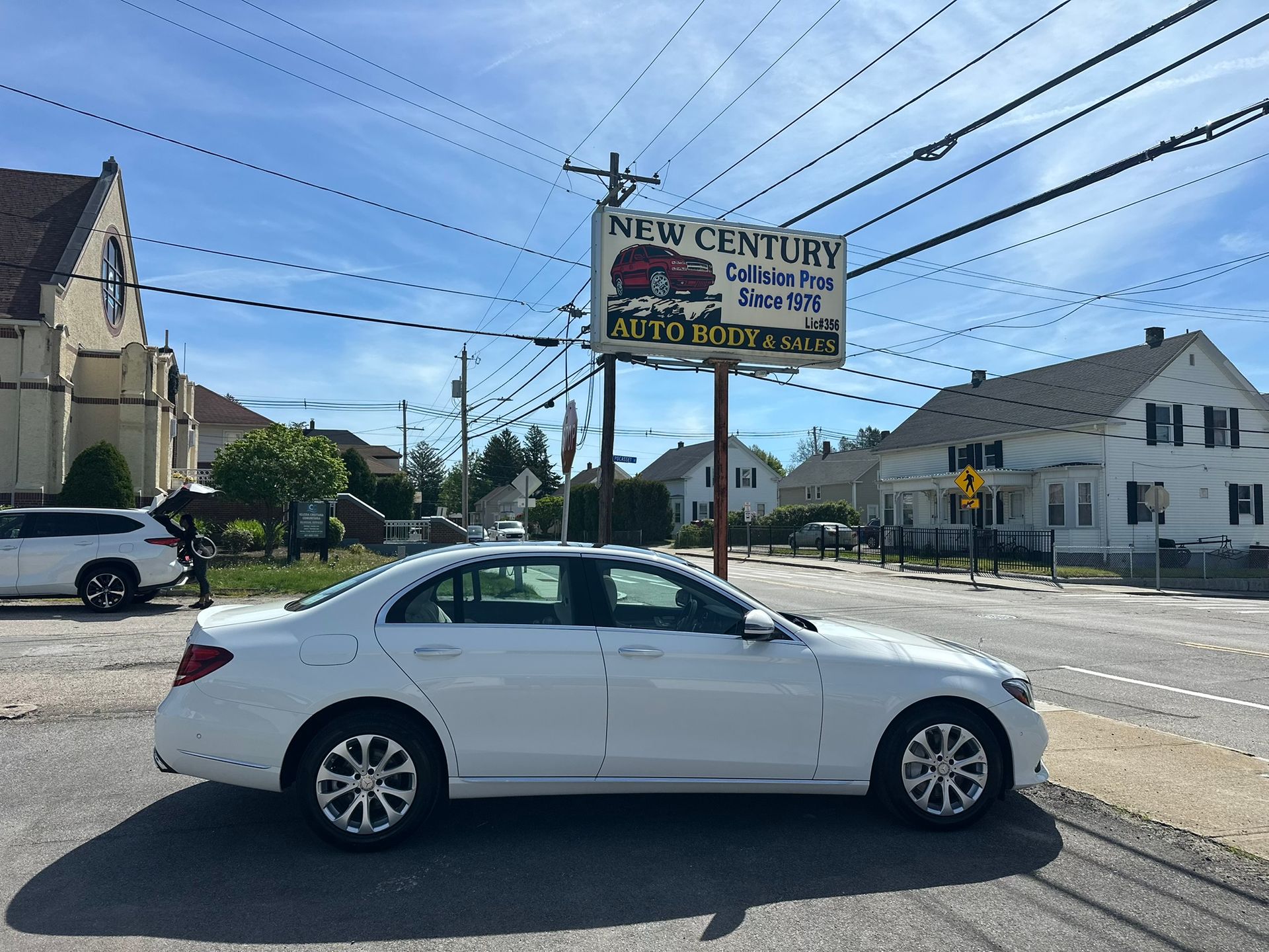 White sedan parked by roadside near a New Century auto service sign on a sunny street