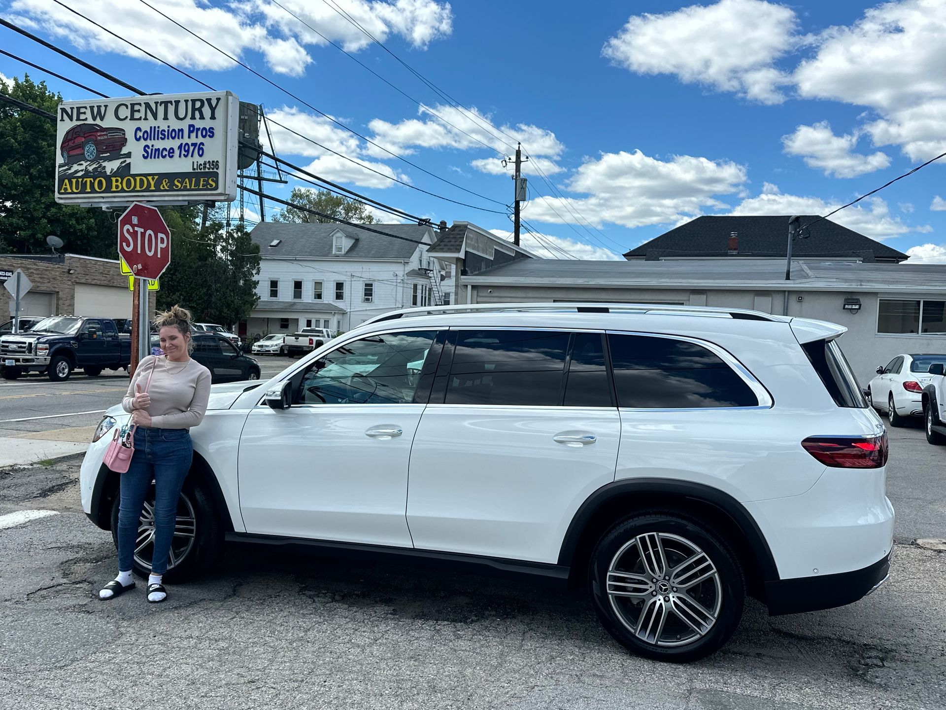 Person standing beside a white SUV in a parking lot under a blue sky with clouds.