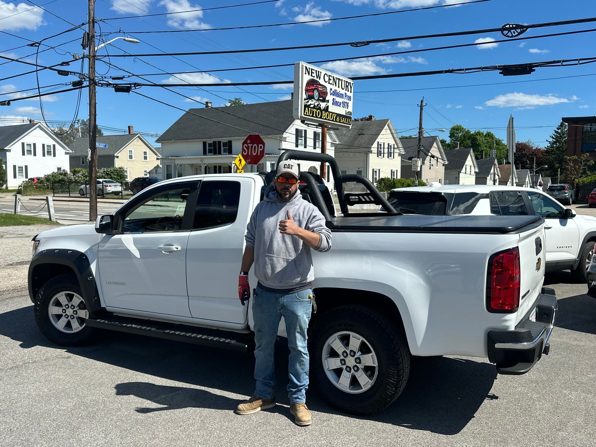 Person leaning on a white pickup truck on a sunny street near houses and power lines