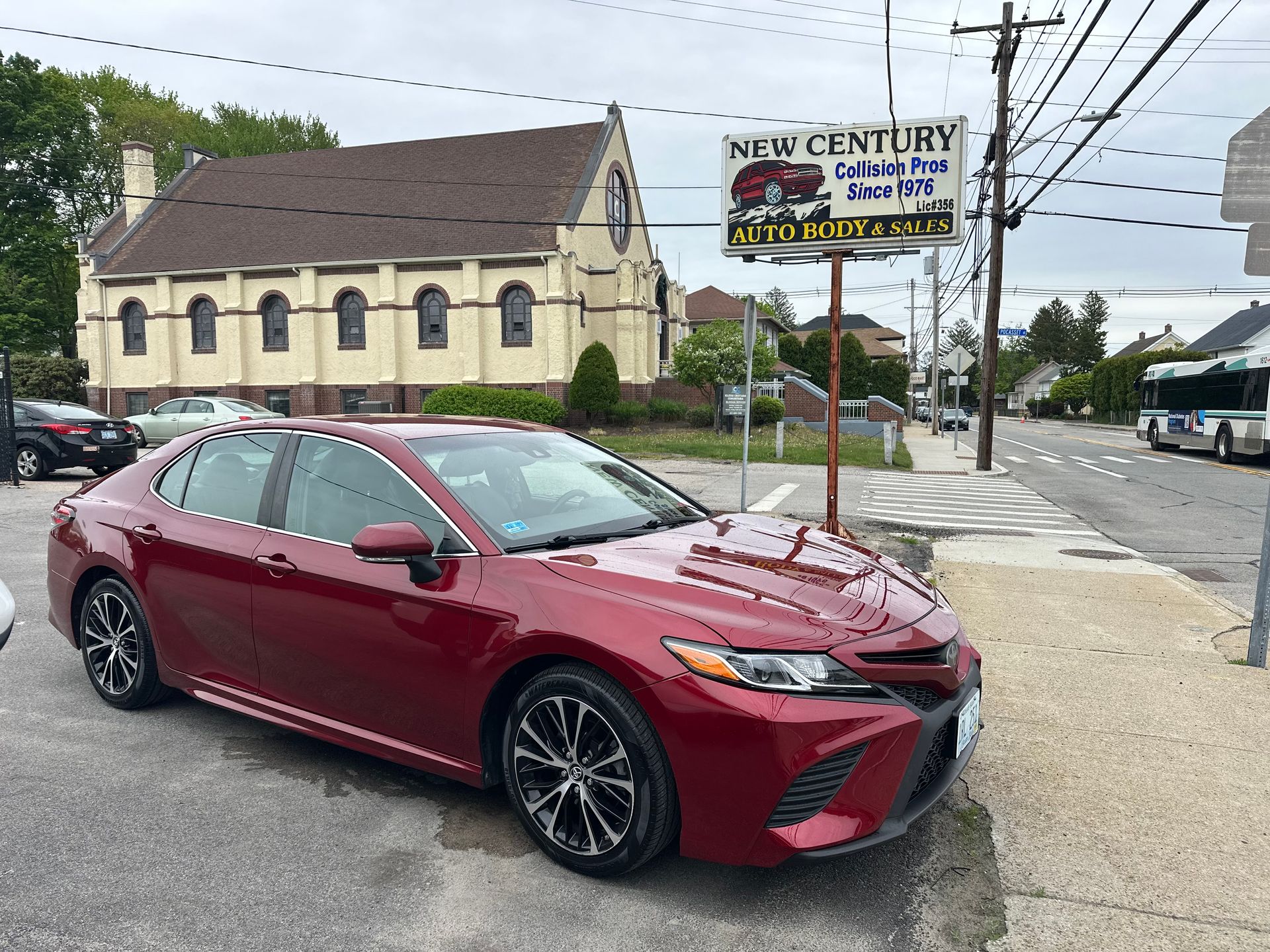 Maroon sedan parked near a street corner by a New Century sign and beige building