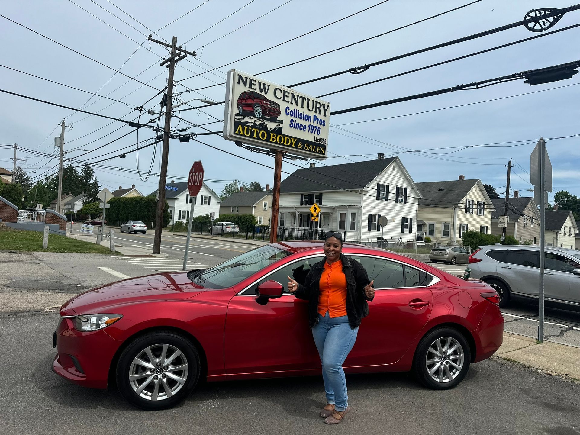 Person standing by a red sedan at a car lot with a New Century sign overhead