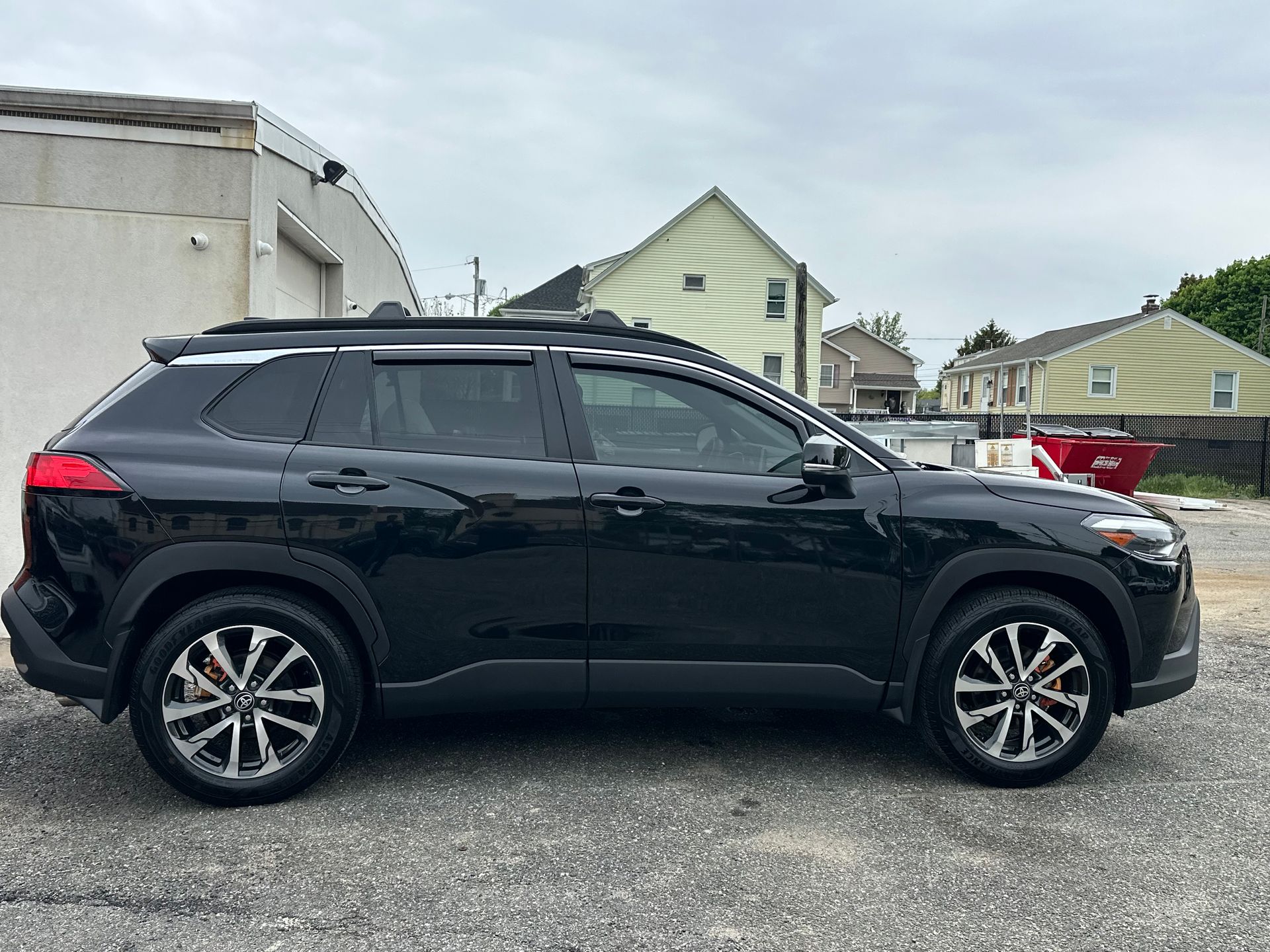 Black SUV parked in a lot beside houses, side view.