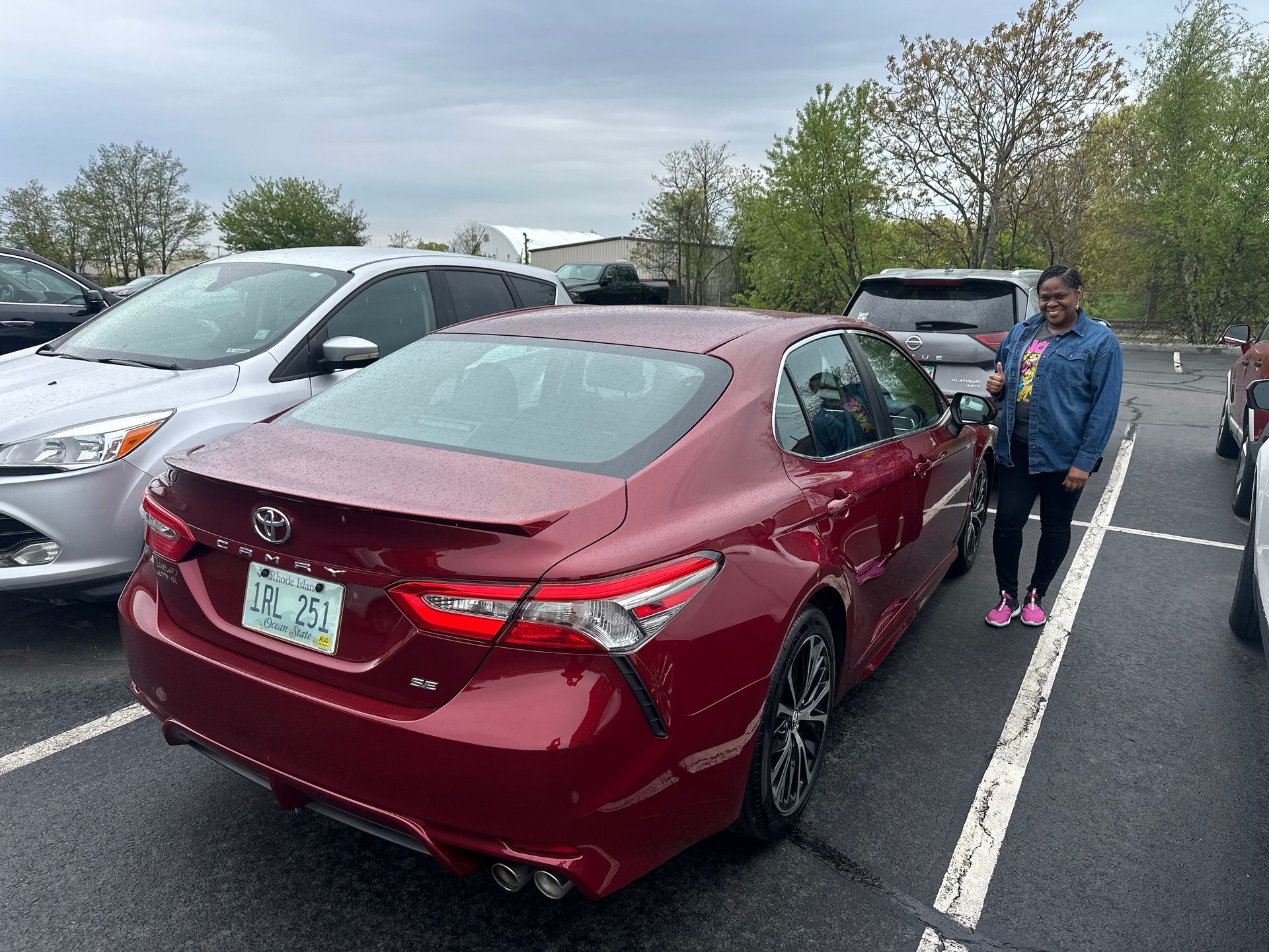 Red Toyota sedan in a parking lot beside a person in a blue jacket and gray pants.
