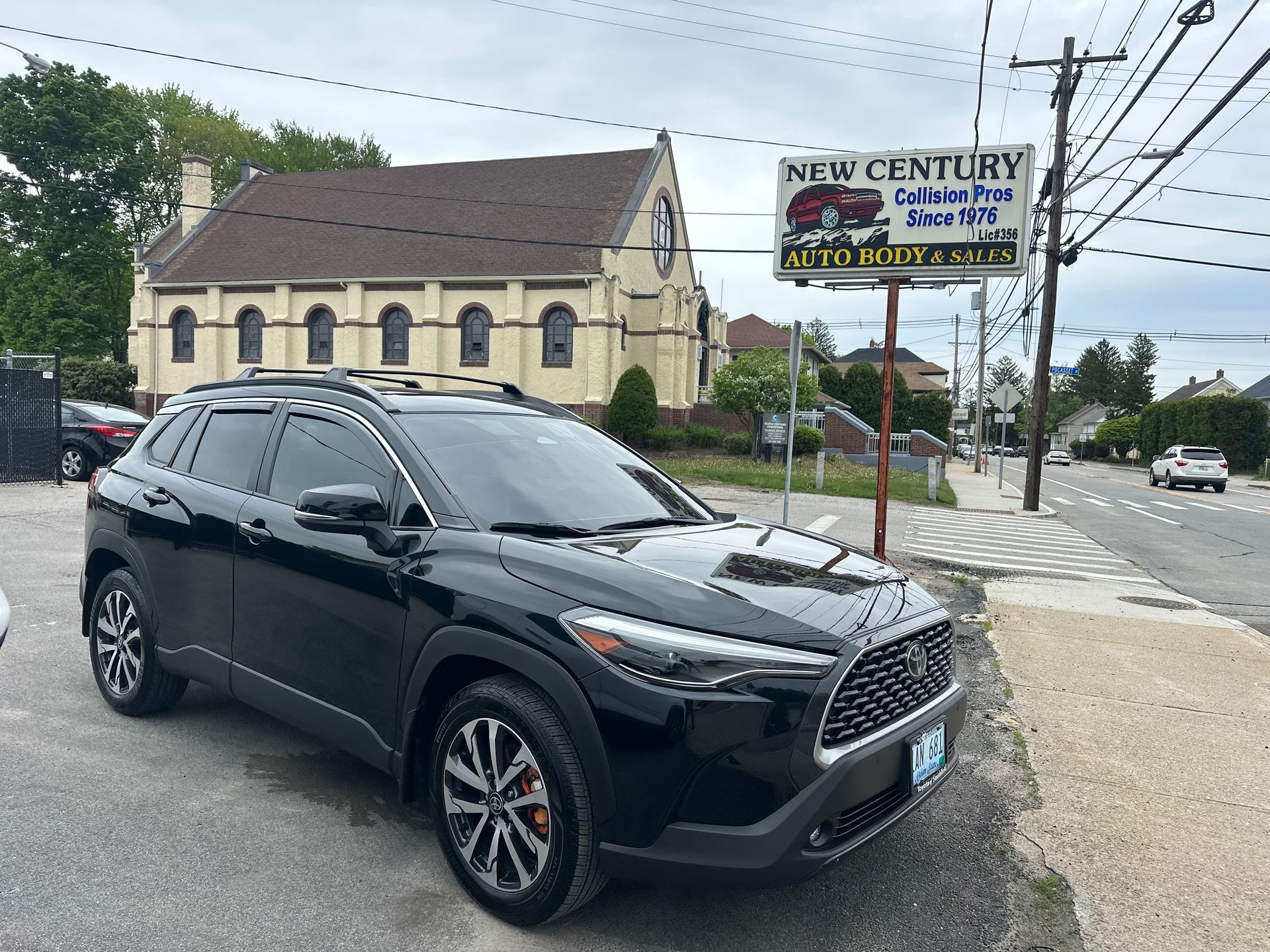 Black SUV parked on a street corner near a storefront sign and beige building.