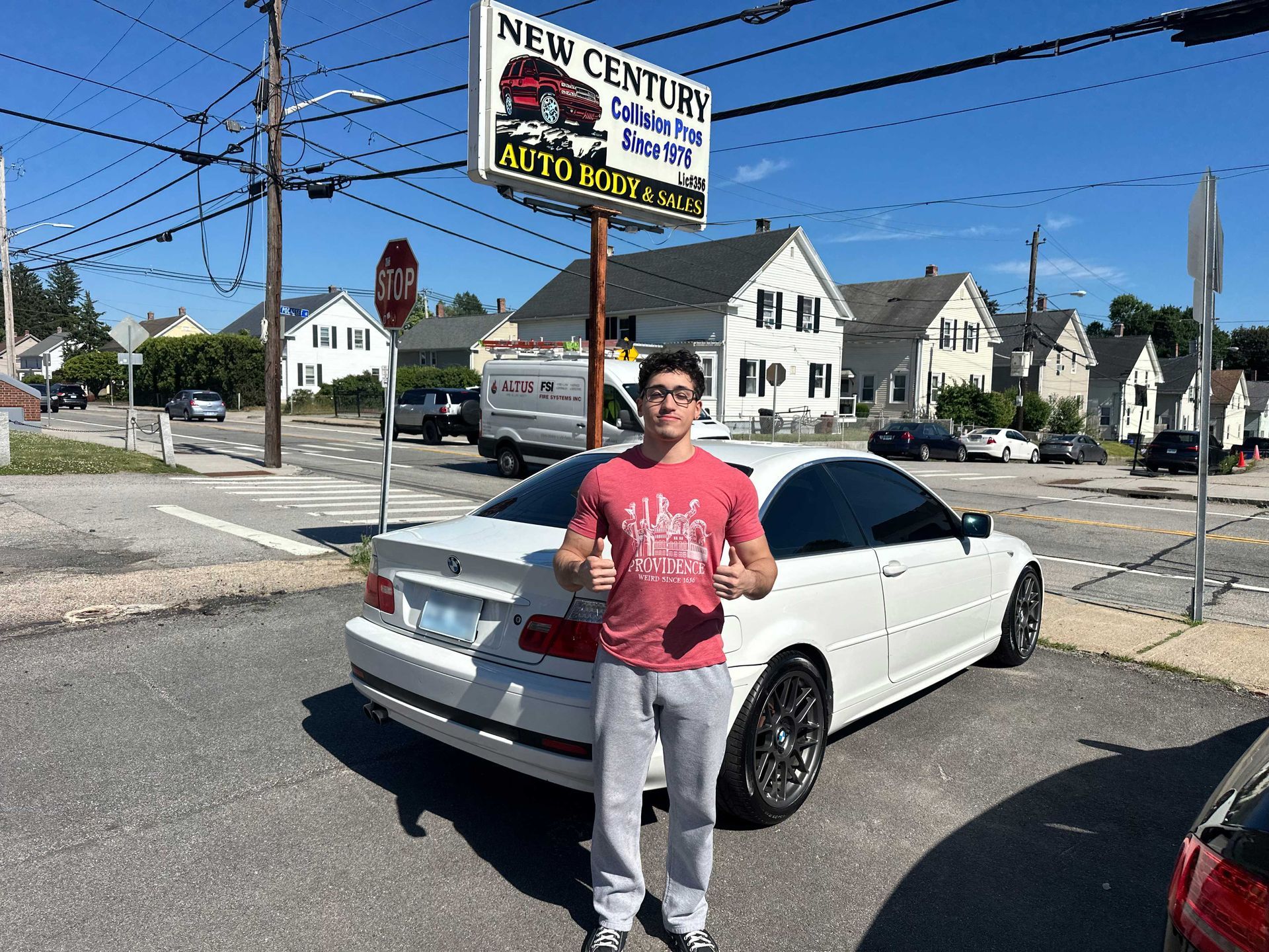 Man standing beside a white sedan at a street intersection under a sign