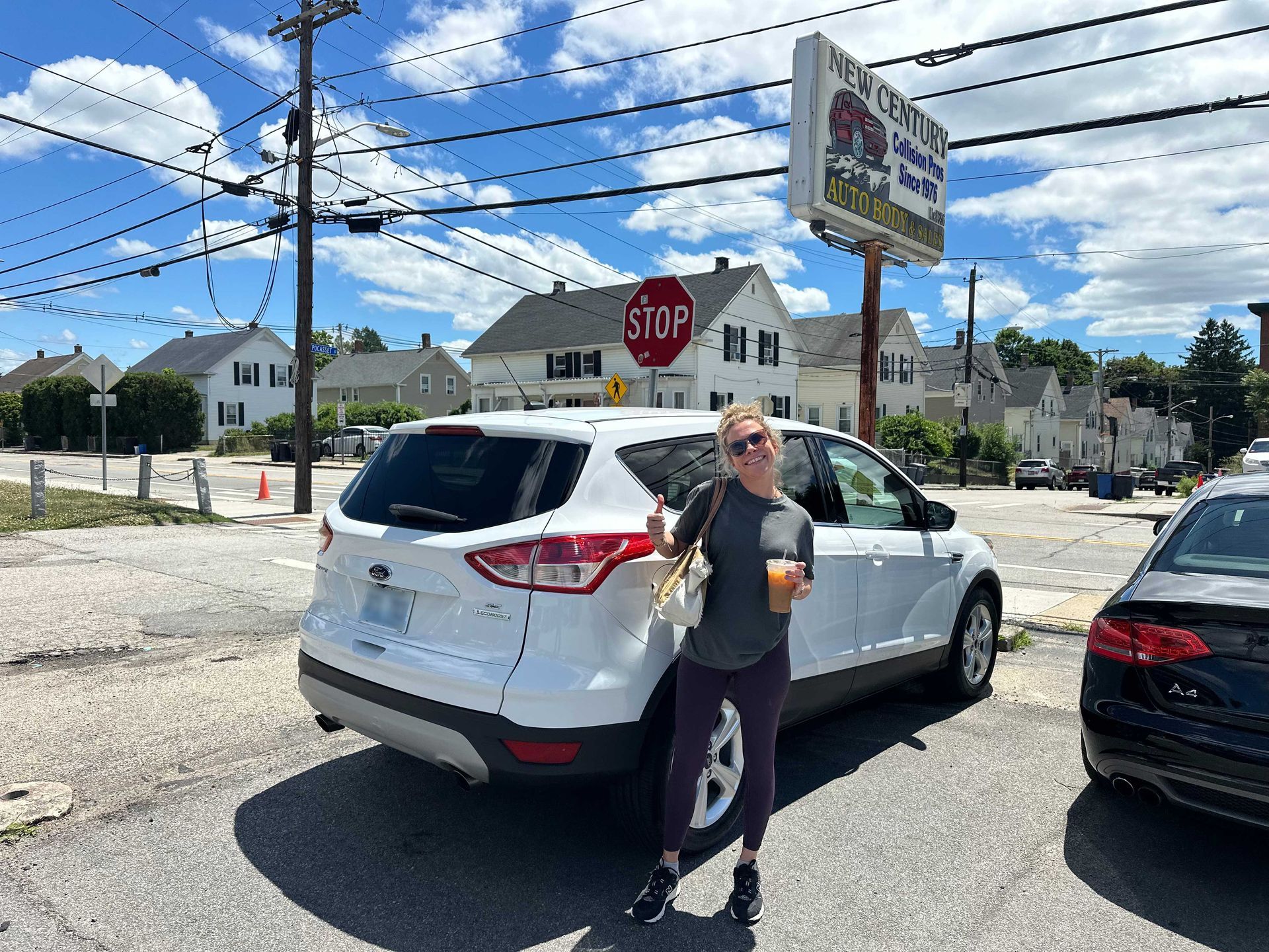 Person standing by a white SUV near a stop sign at a parking lot intersection under a cloudy sky