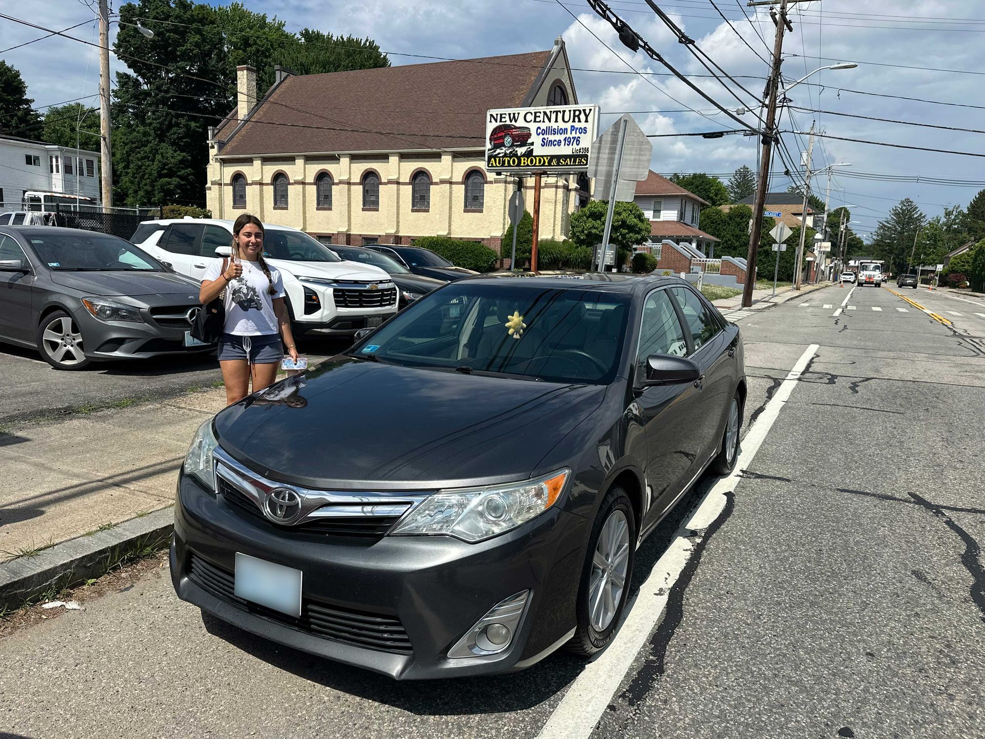 Woman standing by a black sedan on a city street near a yellow building