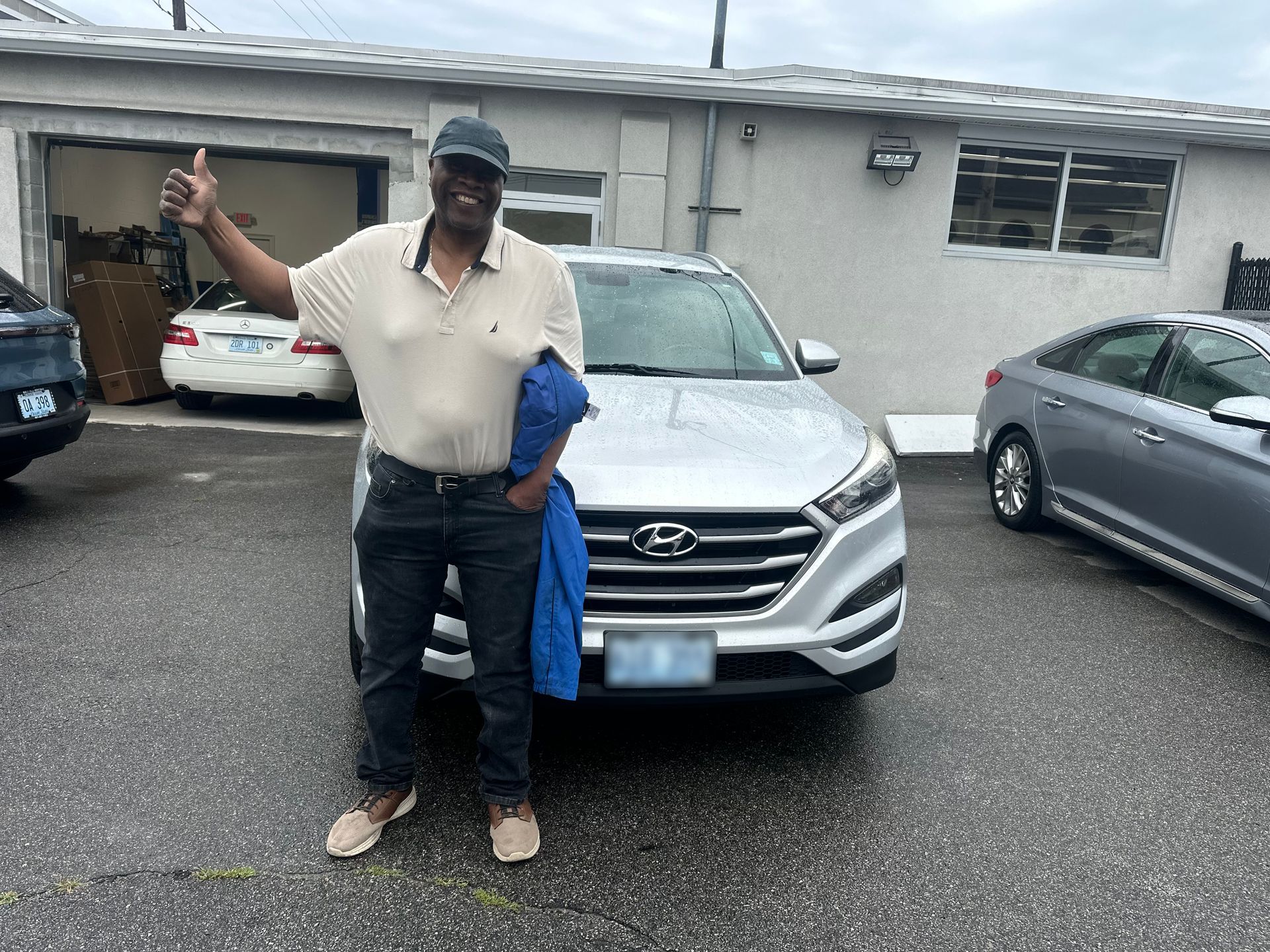 Man standing in front of a silver SUV in a parking lot, raising one arm and holding a blue cloth.