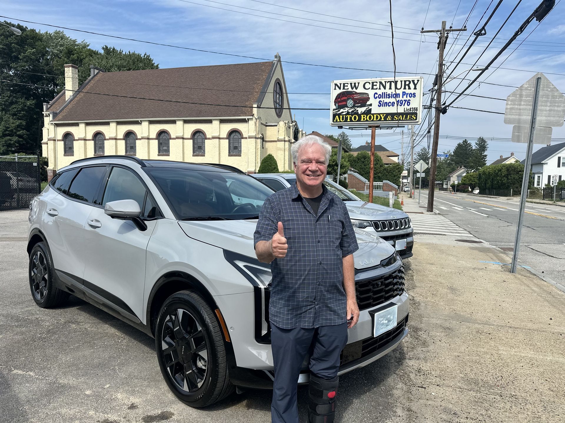 Man standing beside a white SUV, giving a thumbs-up in a car lot.
