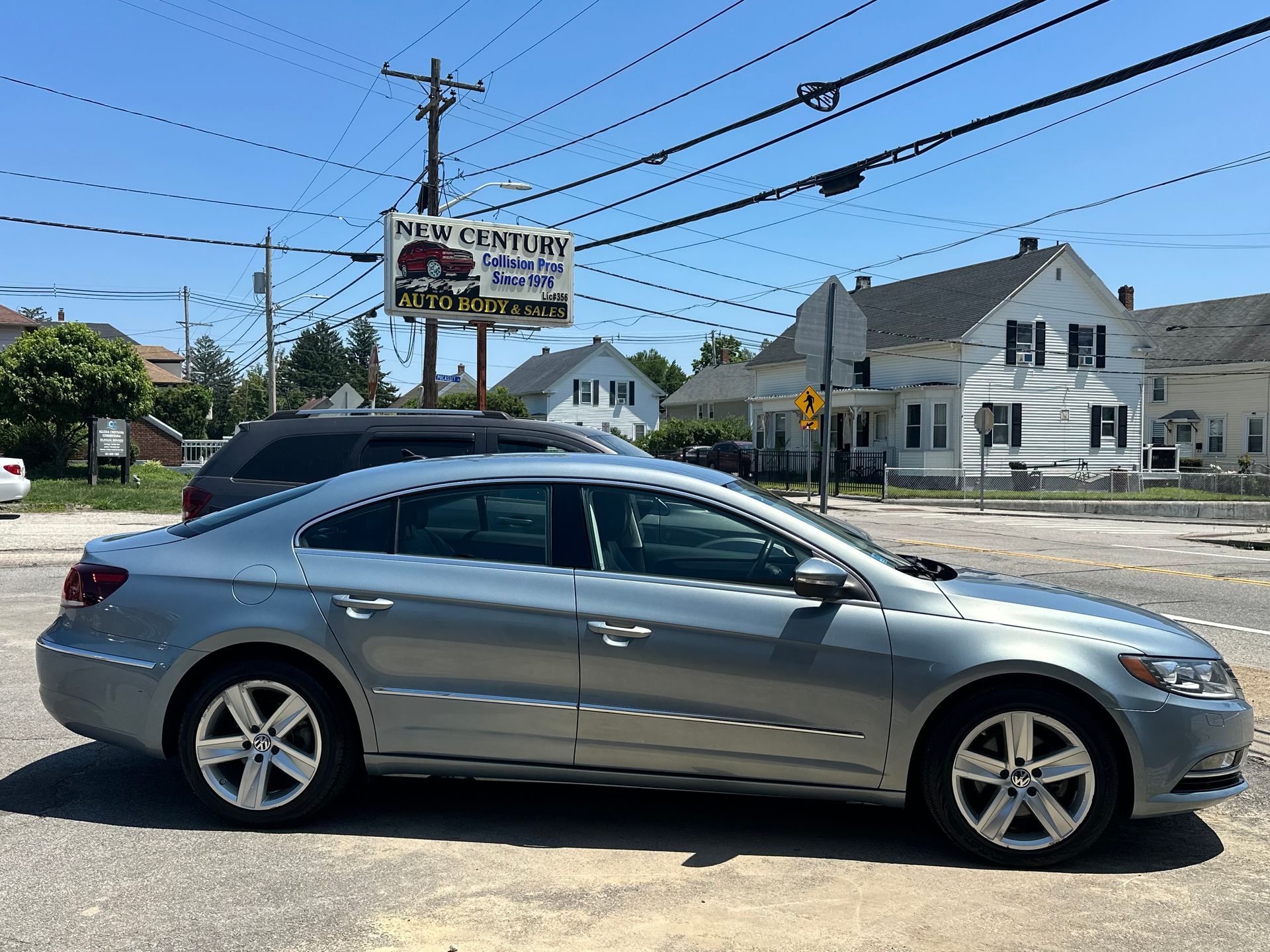 Silver sedan parked on a sunny street near houses and a roadside sign under power lines