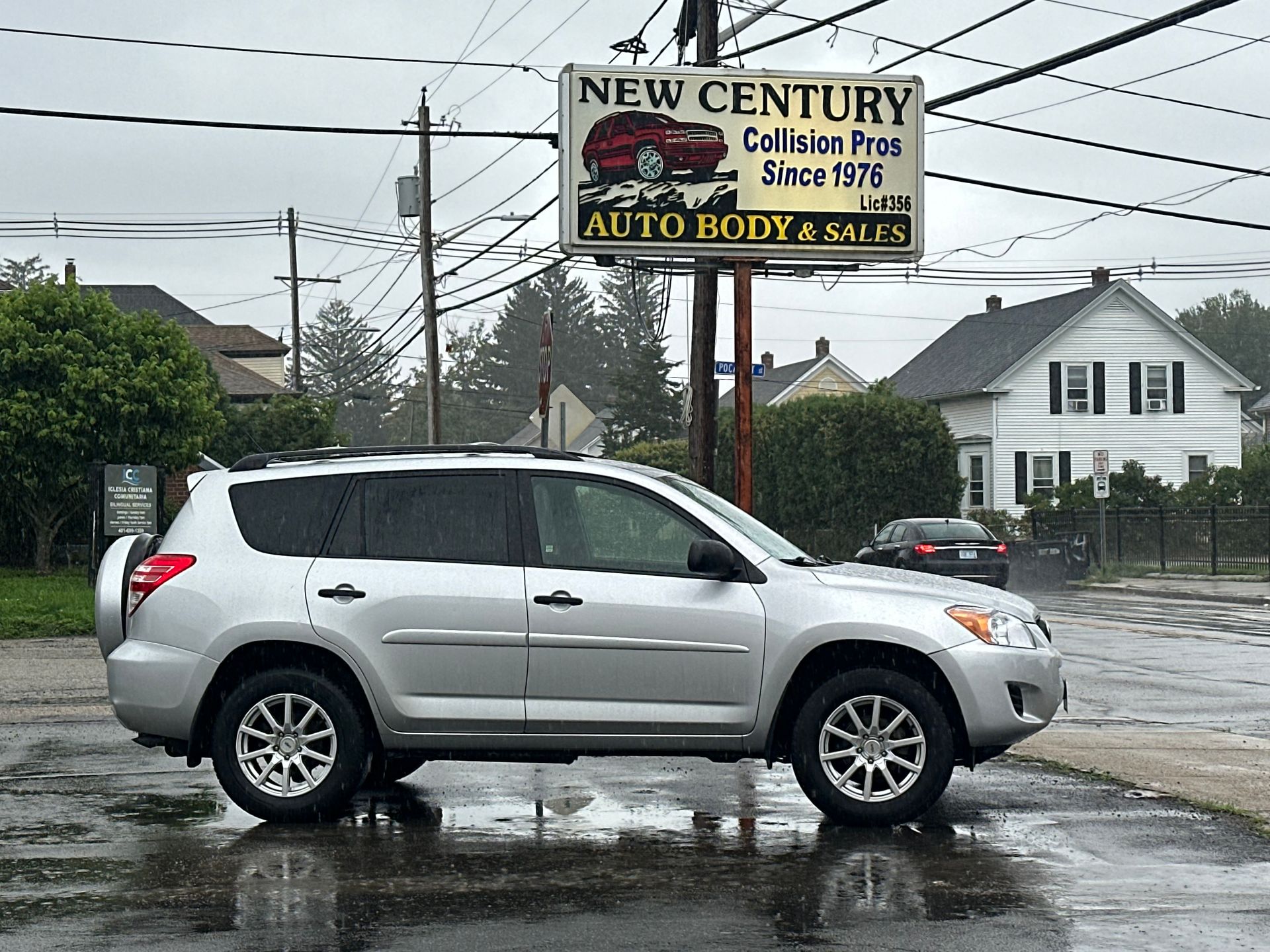 Silver SUV parked on a wet lot in front of New Century Collision Plus auto body shop