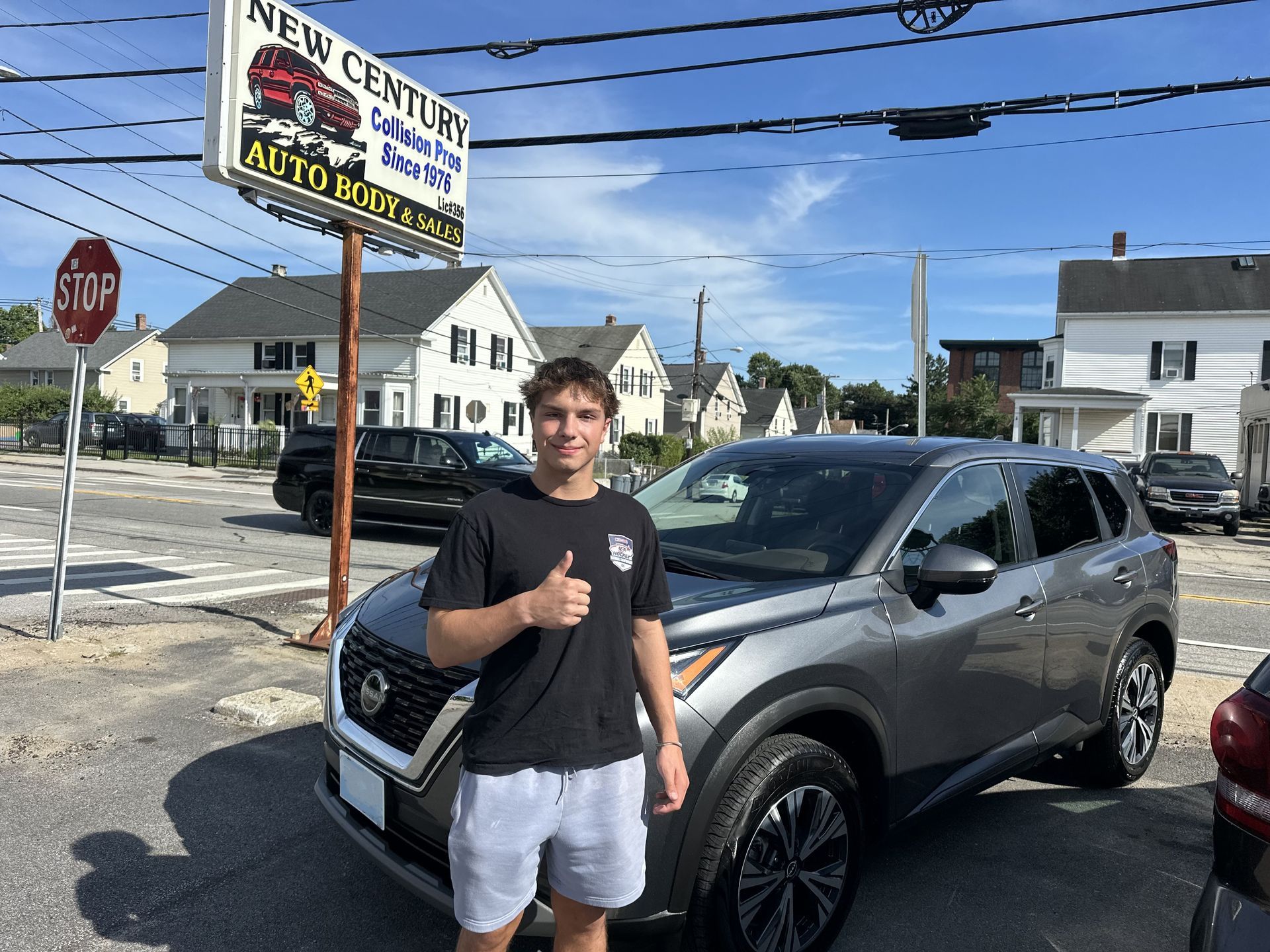 A man standing beside a gray SUV giving a thumbs-up in a sunny parking lot.