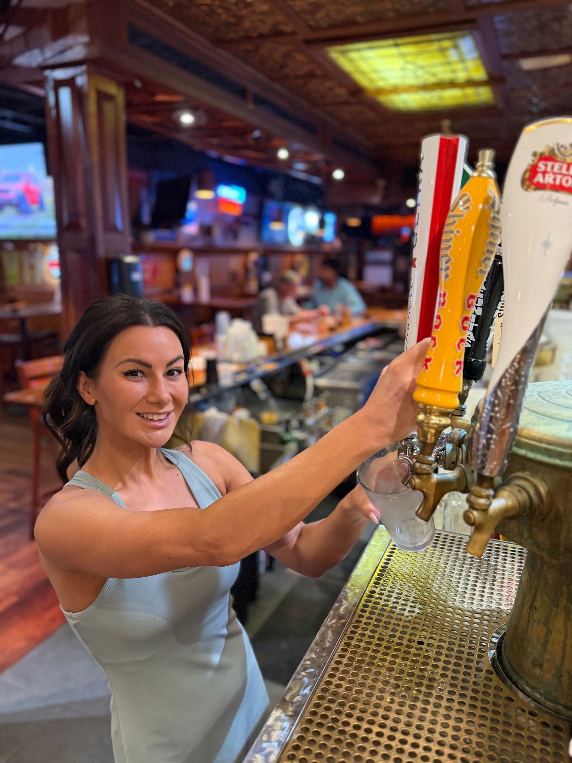 A Rooster's Bar & Grill Team member pouring beer at a bar tap, smiling in a lively restaurant setting.