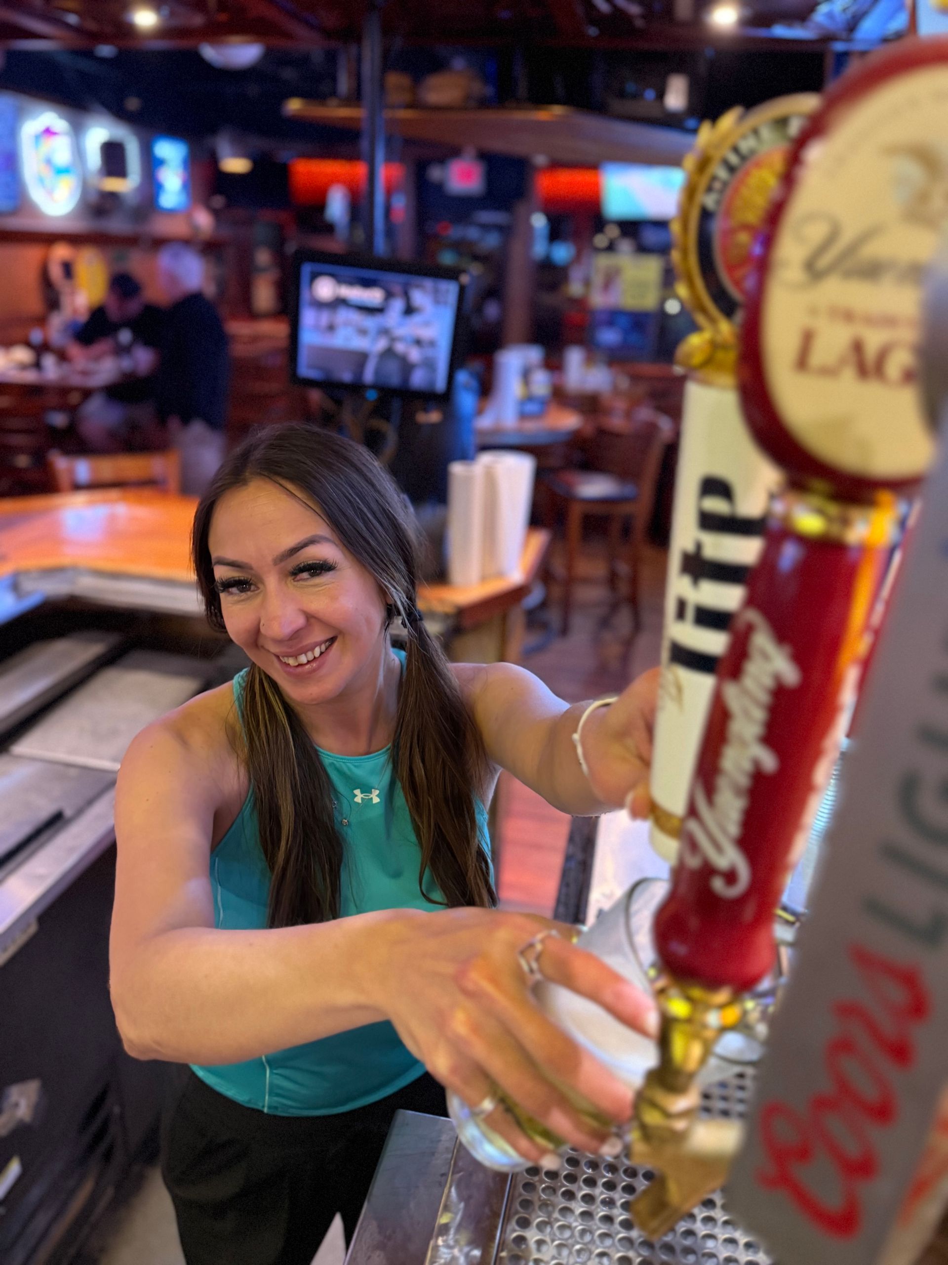 A Rooster's Bar & Grill Team member smiling and holding a giant beer in a lively bar at night