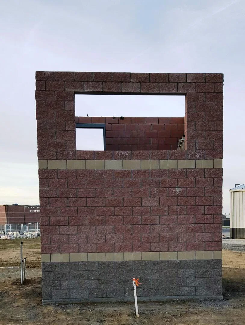 Brick building facade with window cutouts. Red and grey bricks. Outdoors in field.