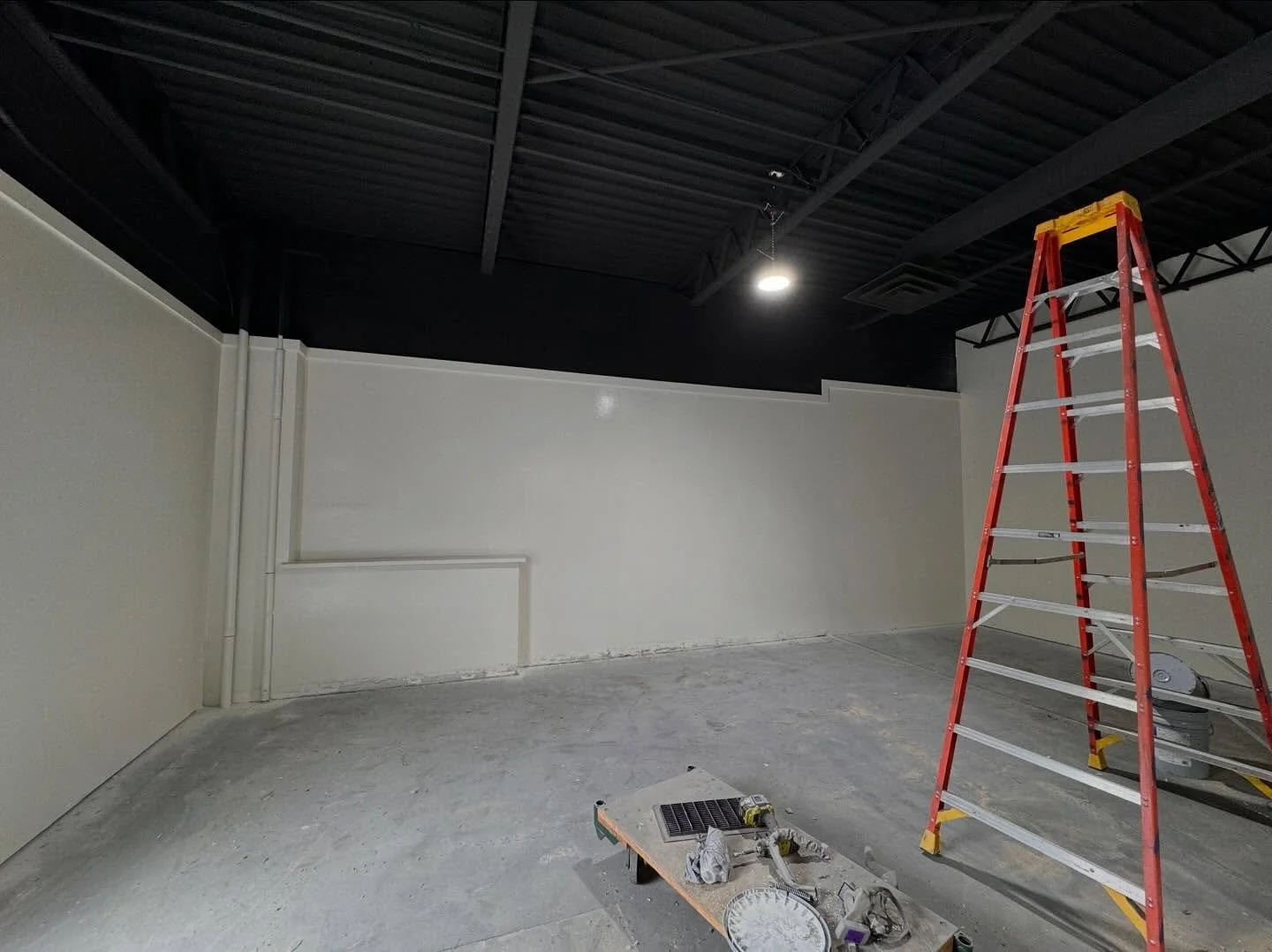 Interior construction: white walls, black ceiling, red ladder, tools, gray concrete floor.
