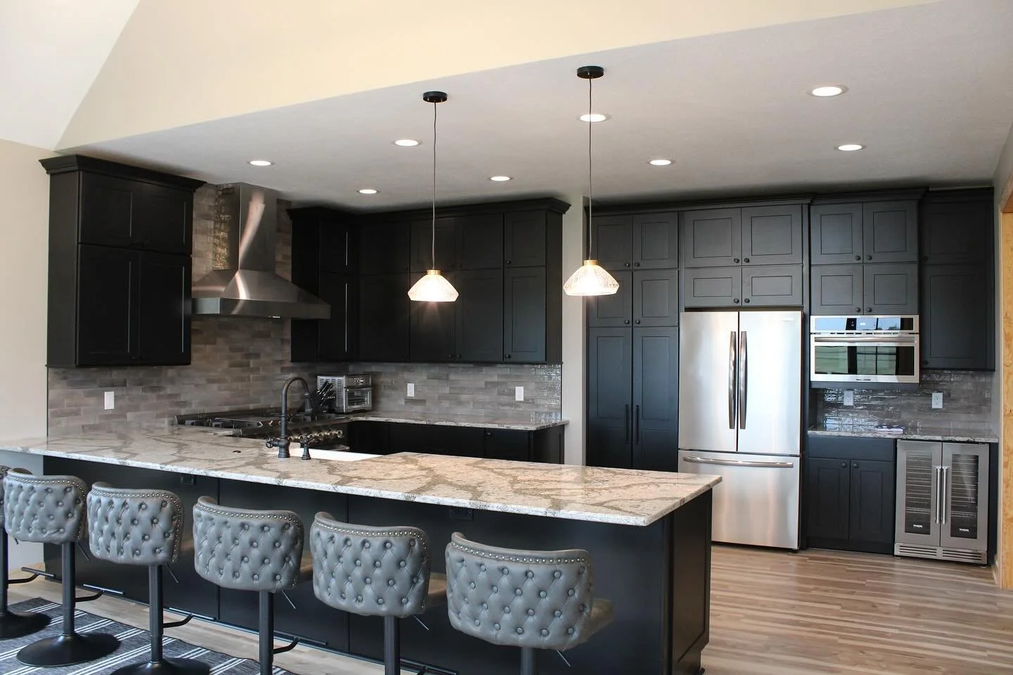 Modern black kitchen with granite island, stainless steel appliances, and gray bar stools.