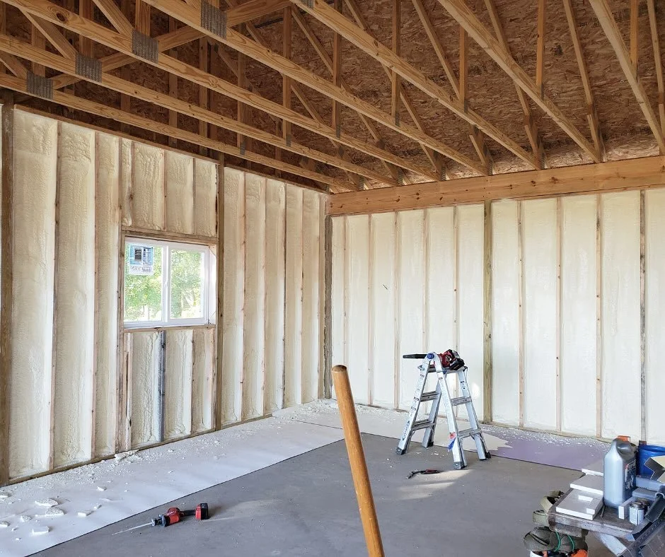 Interior view of a building under construction with walls insulated with foam. A ladder and tools are present.