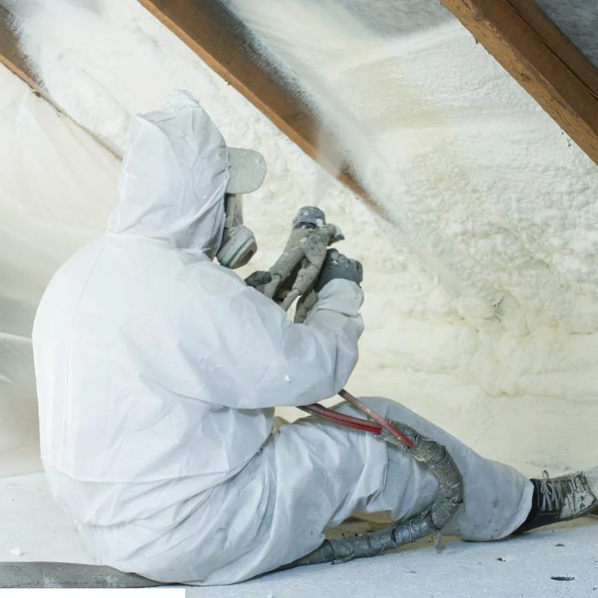 Person in protective suit spraying insulation in an attic.