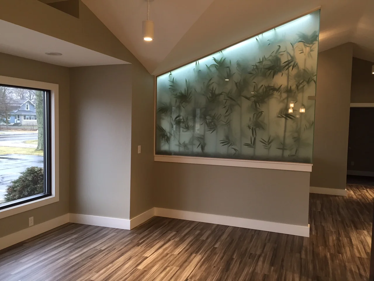 Empty room with a large glass wall with bamboo-like designs, wooden floors, and a window.