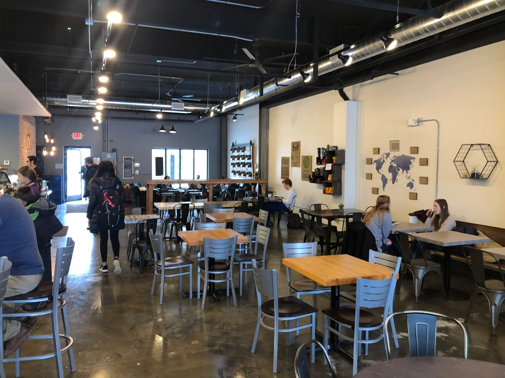 Interior of a coffee shop: tables, chairs, people, a world map, and a black and white color scheme.
