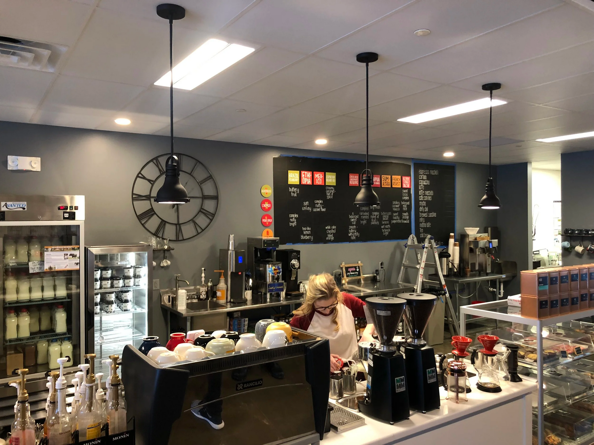 Coffee shop interior with barista behind the counter, menu on chalkboard, and overhead lights.